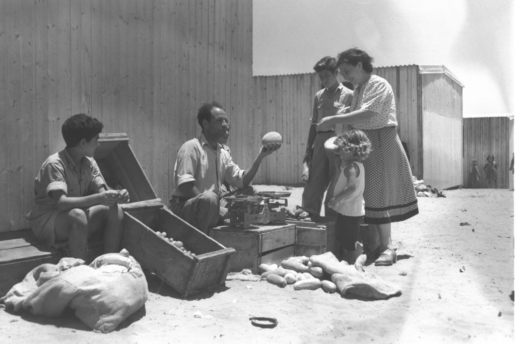 Mrs. Pliska, a new immigrant from Bessarabia (today Moldova/Ukraine) buys vegetables from Eliahu Abraham, a former actor from Baghdad, at the maabara (immigrant camp) in Kiryat Ono, summer 1951 (Teddy Brauner, GPO)