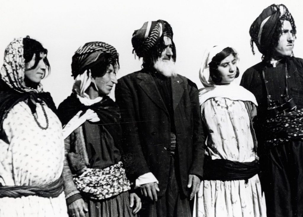 A black-and-white photograph of family members standing in a line, wearing traditional clothing: robes, turbans with tassels and headscarves